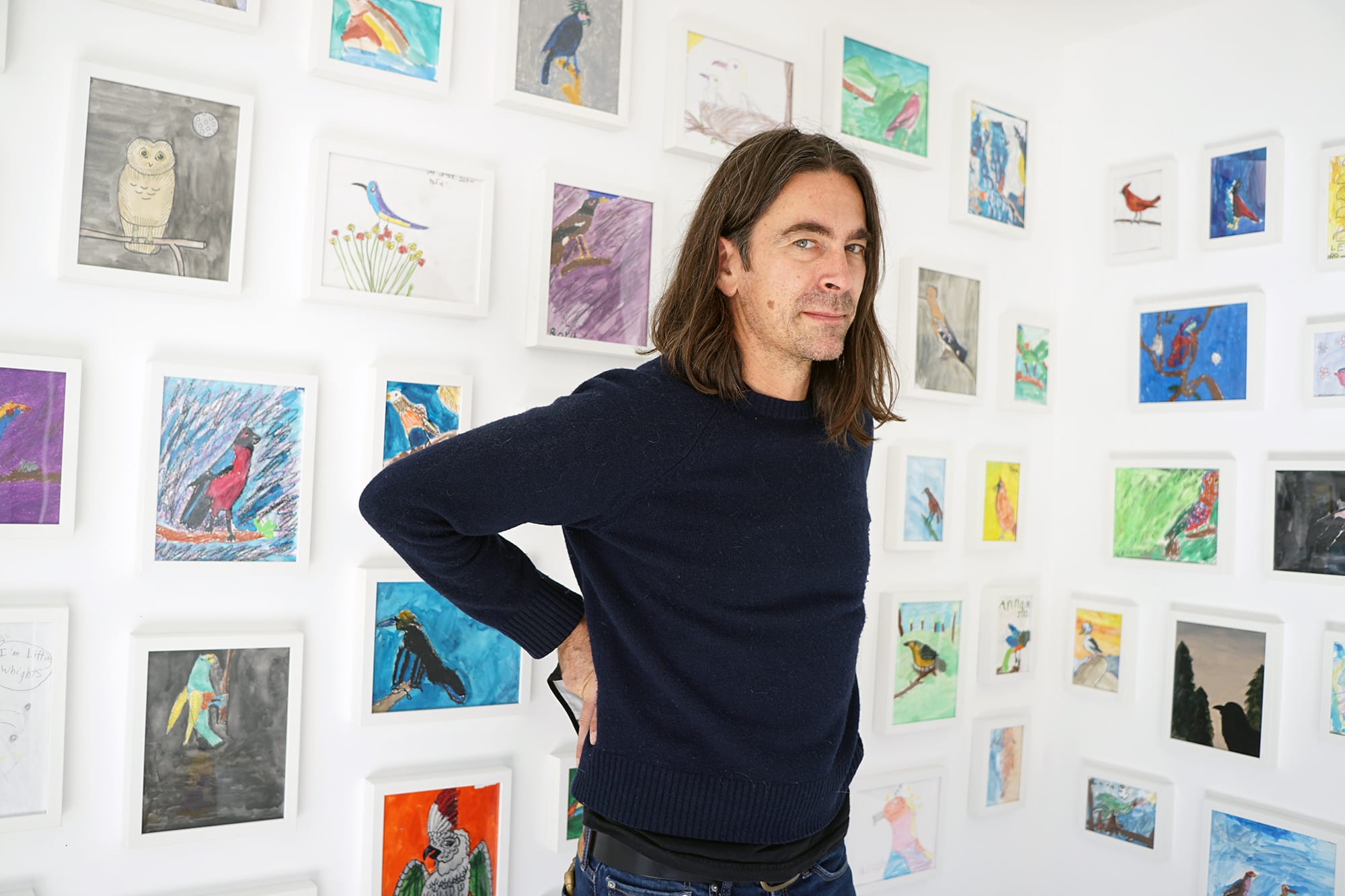 Man in black T-shirt in front of wall with small colorful paintings