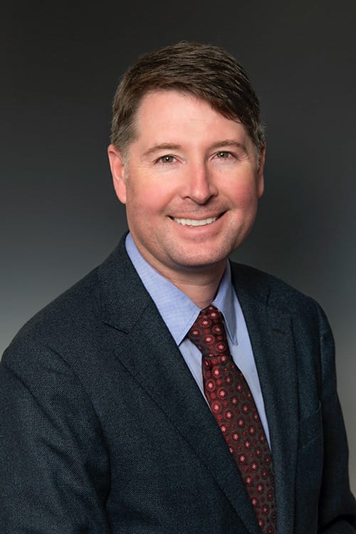 A man in a tie and suit jacket faces the camera