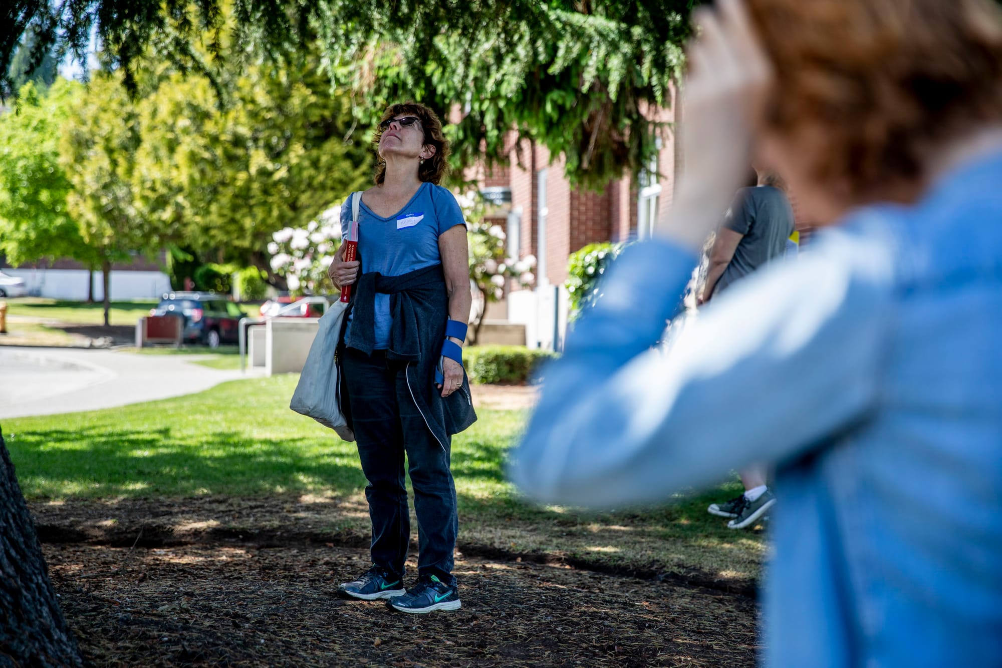 Kelley McHenry of Shoreline looks up into a tree as a group of volunteers learn about identifying majestic or exceptional trees, meaning trees with a trunk diameter of 30 inches or more, at Magnuson Park in Seattle on May 19, 2019. (Photo by Dorothy Edwards/Crosscut)