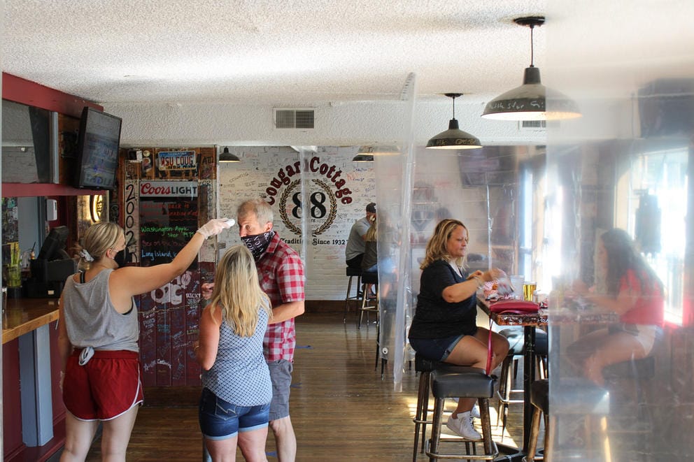 Customers and staff inside a bar with sheets of plastic separating tables