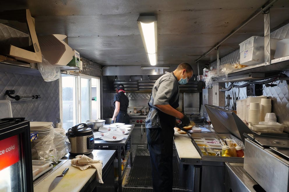 Two people prepare food inside a small food truck