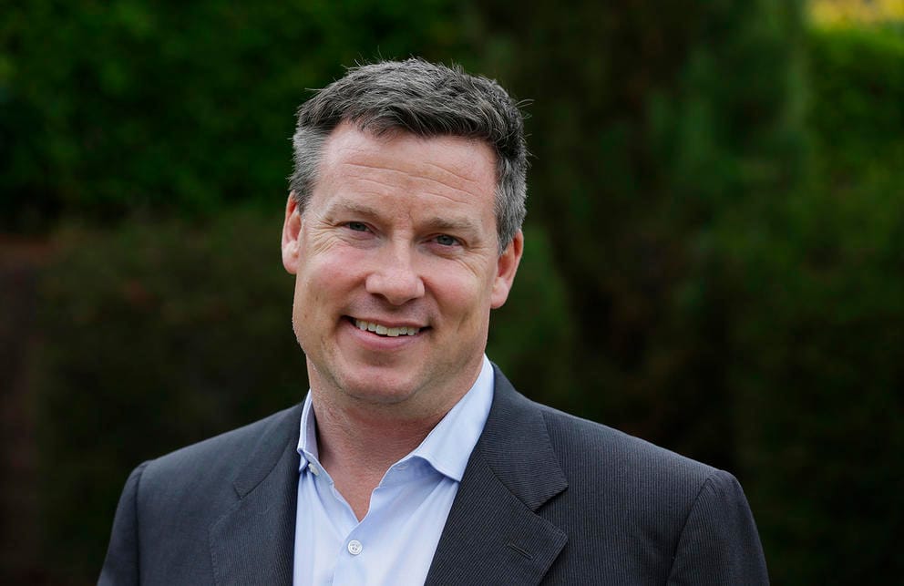 Mark Mullet smiles in a portrait against a dark green background.