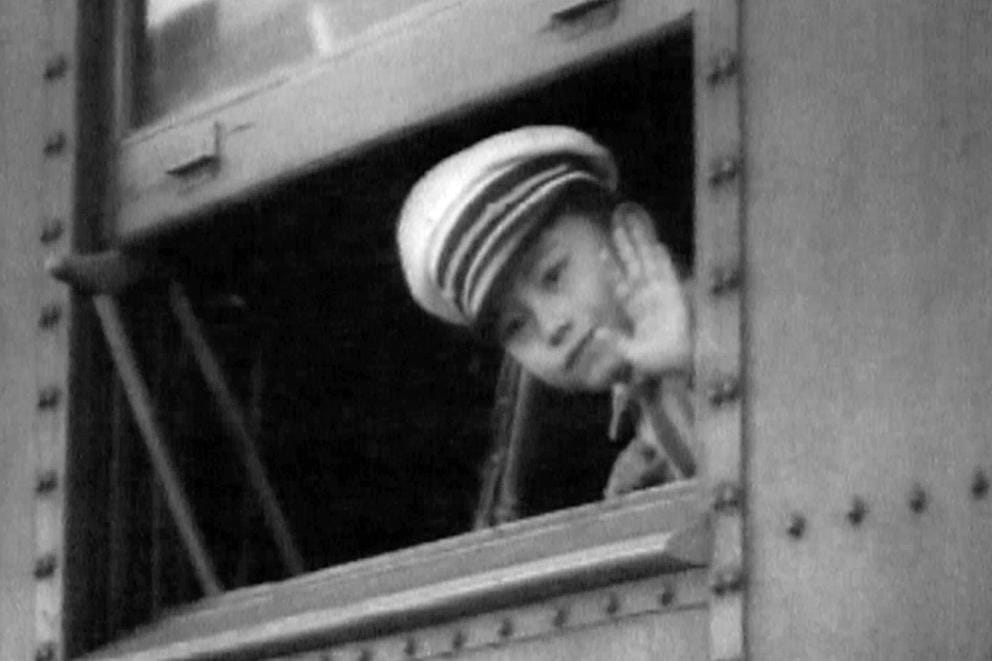 A Japanese American bot is seen waving from a train window.