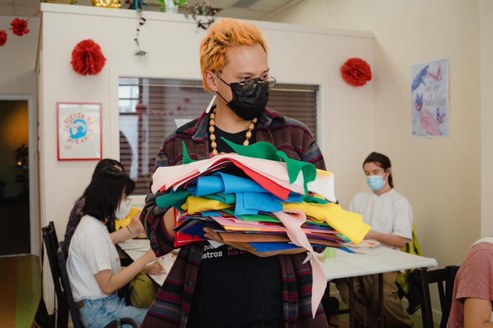 person with orange hair is carrying a stack of colorful fabric
