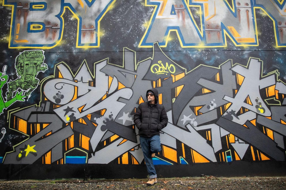 A man stands against a mural covered wall