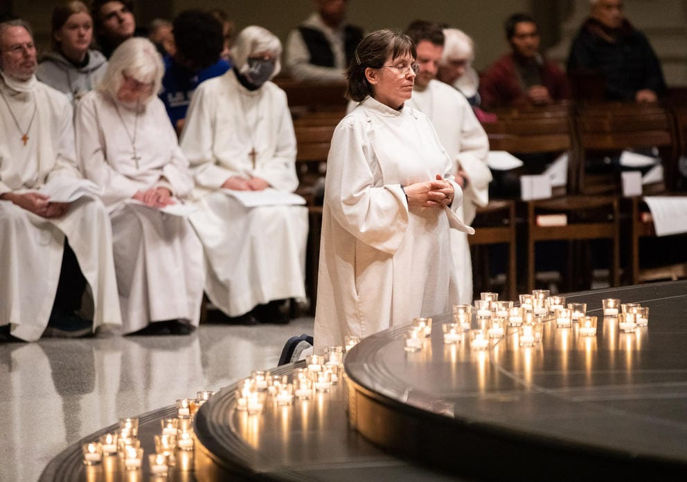 church assistants in white robes kneel and pray in front of lit candles