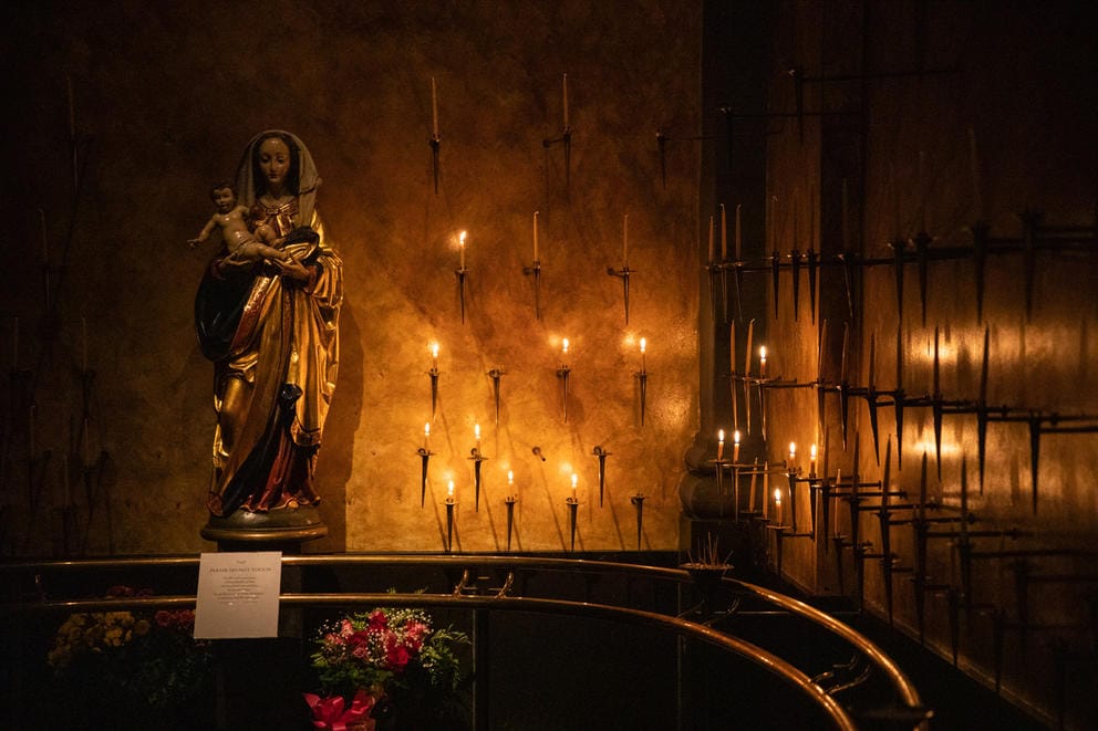 lit candles line a wall outside a cathedral in memorium of homeless people who died