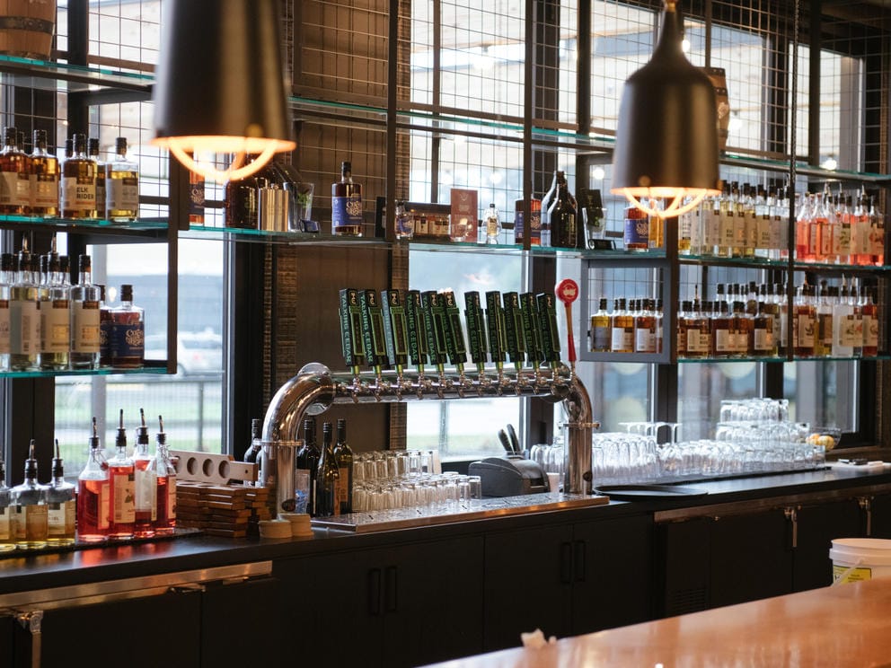 A medium shot of a bar with bottles of liquor on shelves and a line of beer taps