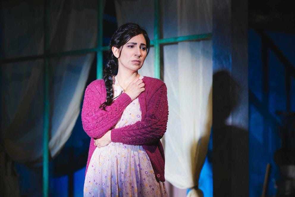 on stage in a theatrical production, a woman stands in front of a window and looks concerned