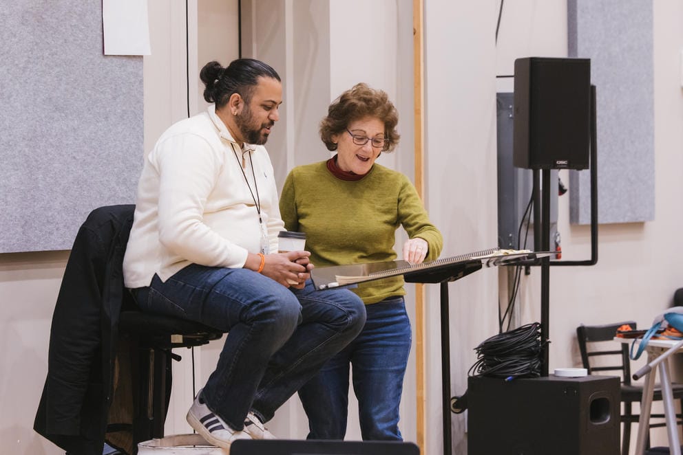 a photo of a man and woman smiling while looking over a score on a music stand