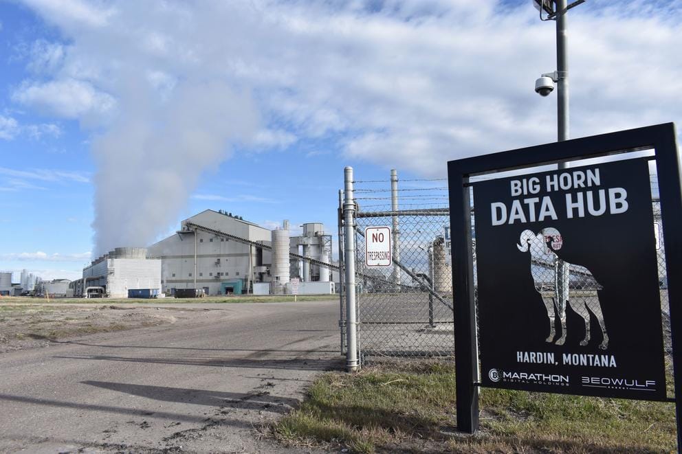 A coal-fired power plant blows smoke behind a sign of the cryptocurrency 