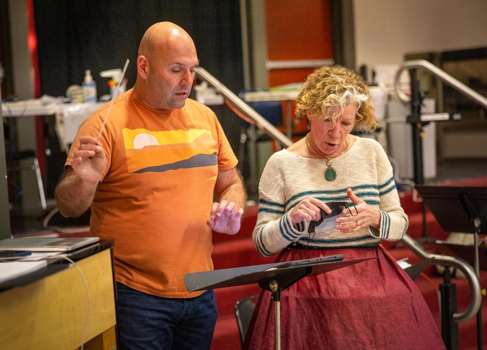 a man (left) and woman backstage, behind a music stand, rehearsing for a musical and singing