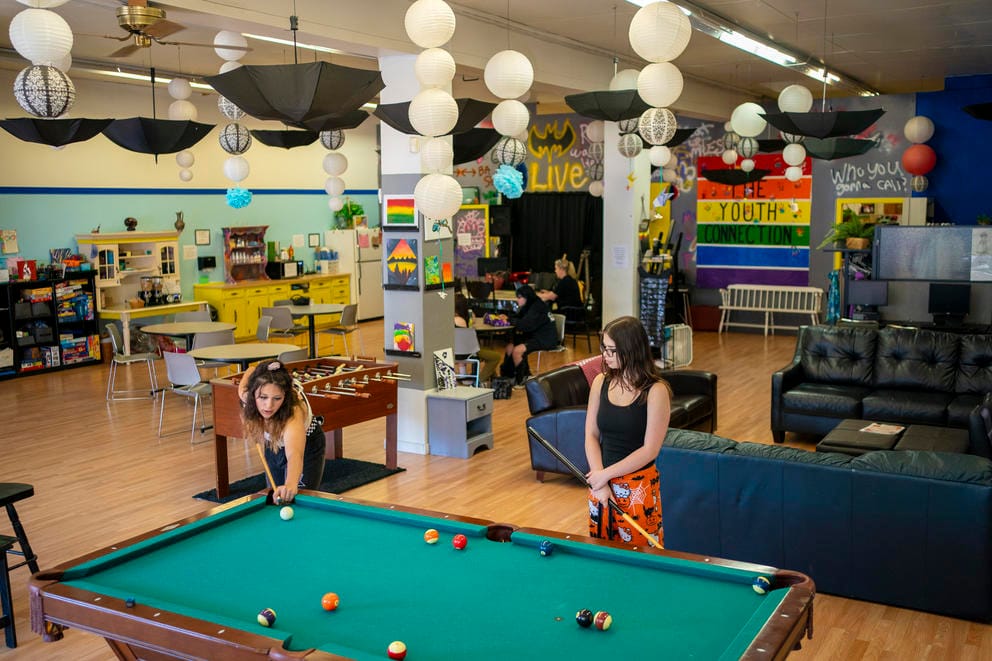 Two teens play pool in a brightly decorated lounge area at The Youth Connection.