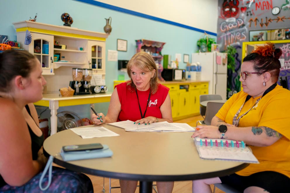 Kirchoff sits between a young client and a staff member at a round table.
