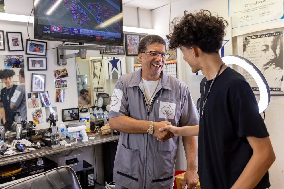 A barber shakes hands with a customer with a mirror in the background.