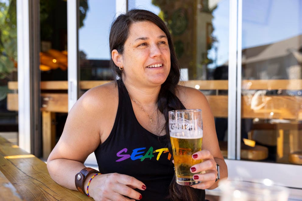 A woman sits outside with a pint of beer in her hand.
