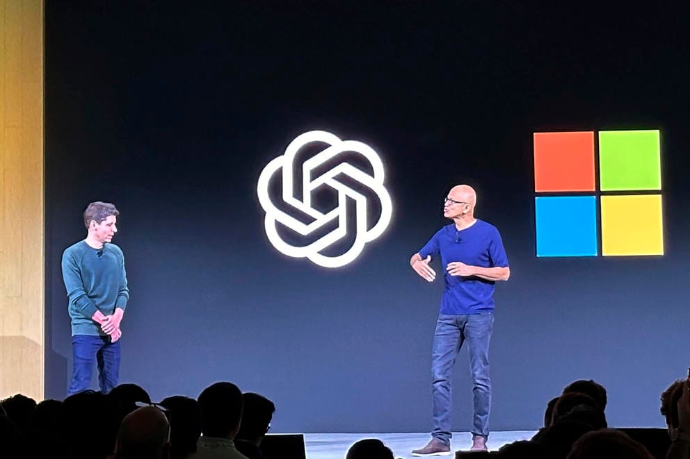 Two people are on a stage in front of a screen displaying the OpenAI and Microsoft logos.