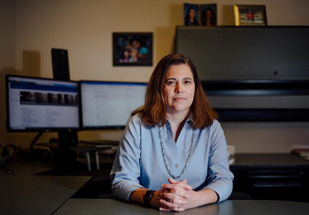 Armijo sits at her desk with her hands clasped and her computer monitor behind her