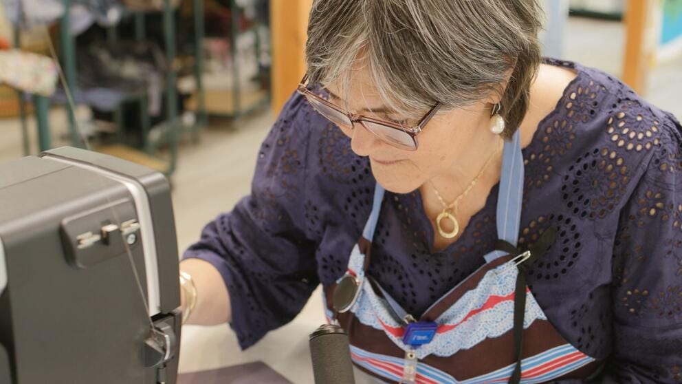 a woman in glasses works at a sewing machine