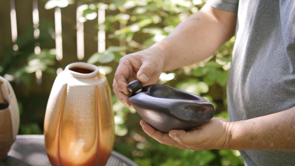 a person holds up a piece of black pottery and lifts up a small clay pebble