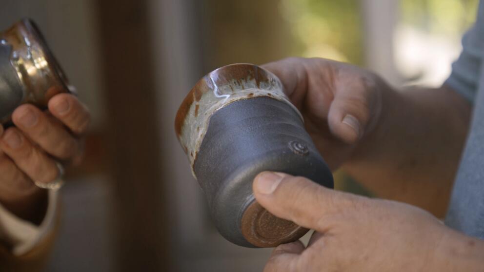 hands hold up a black pottery cup, its edge glazed in milky gray