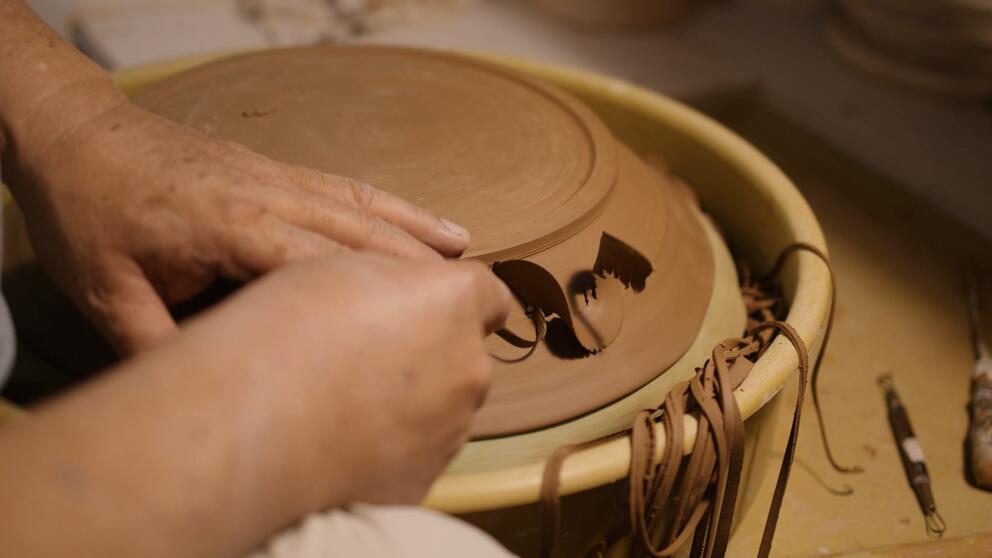 hands at a pottery wheel, trimming brown clay