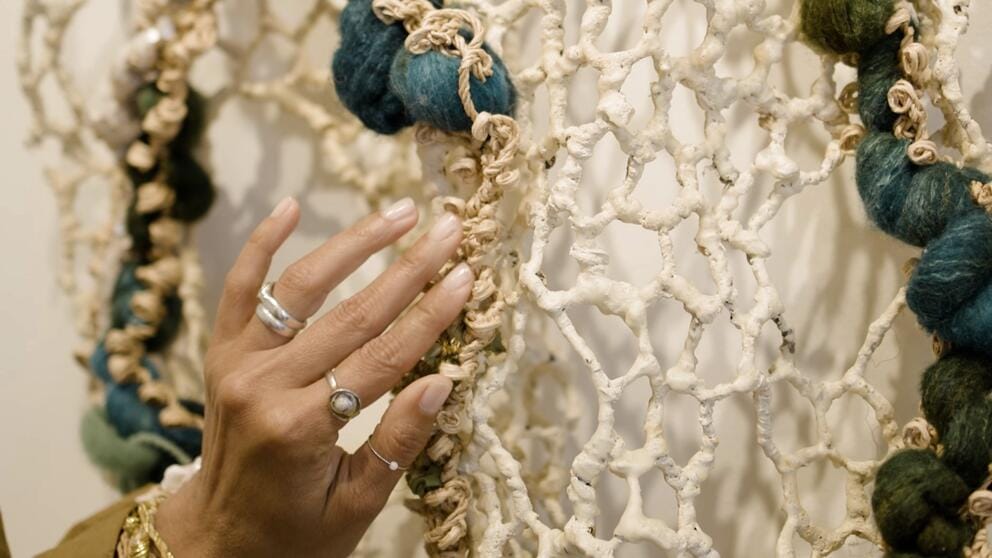 photo of a woman's hand holding a piece of netlike art with puffs of blue and green wool