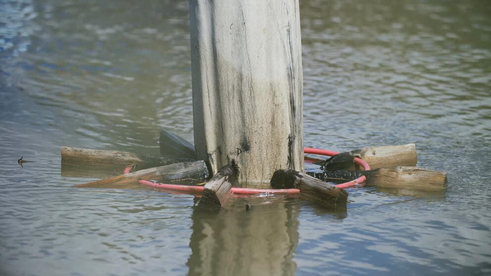 photo of a river piling encircled by a curious device holding sticks of burned wood