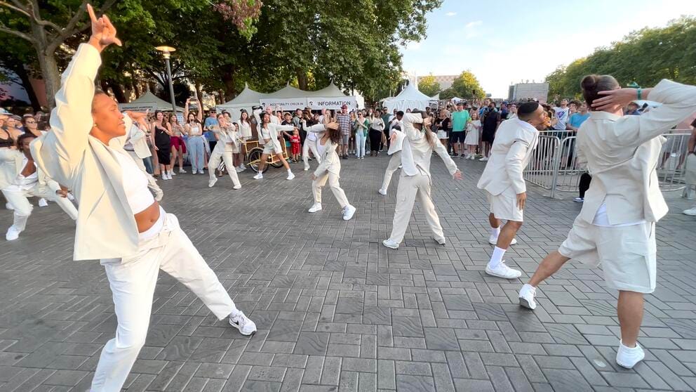 people in white suits dance in a crowded plaza