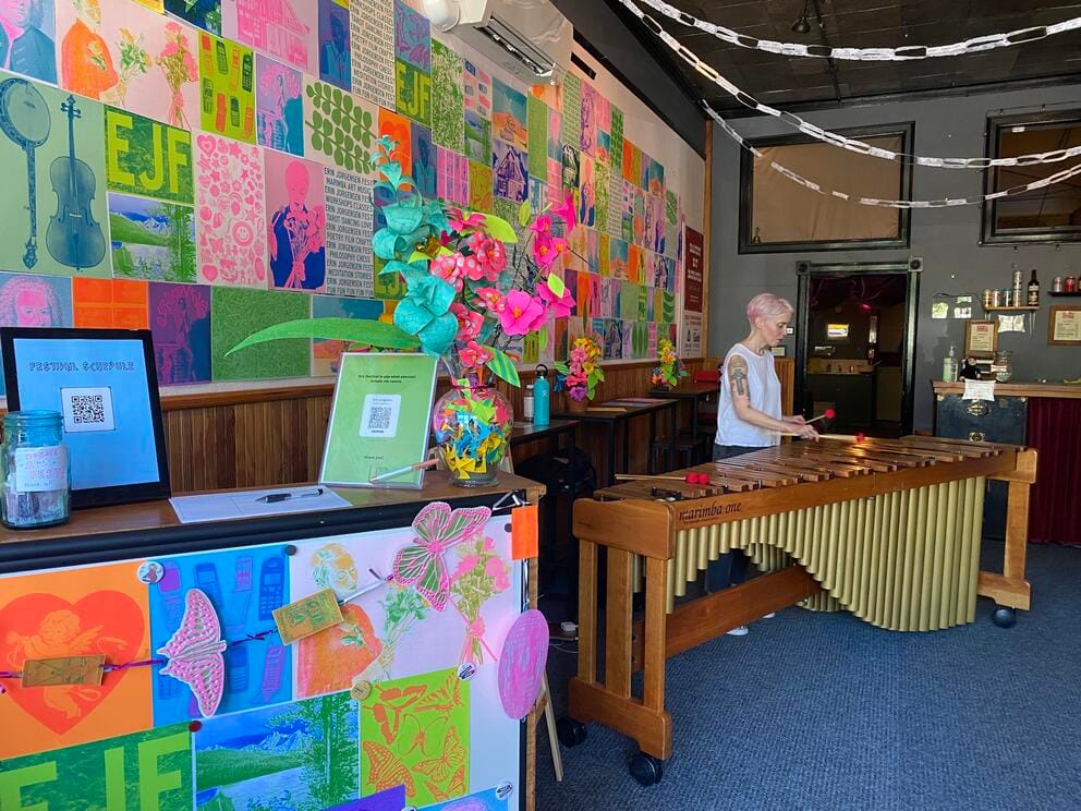 photo of a blond woman playing marimba in a narrow space with colorful posters