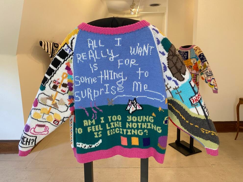 photo of a hand knit sweater on display, with words and images sewn in