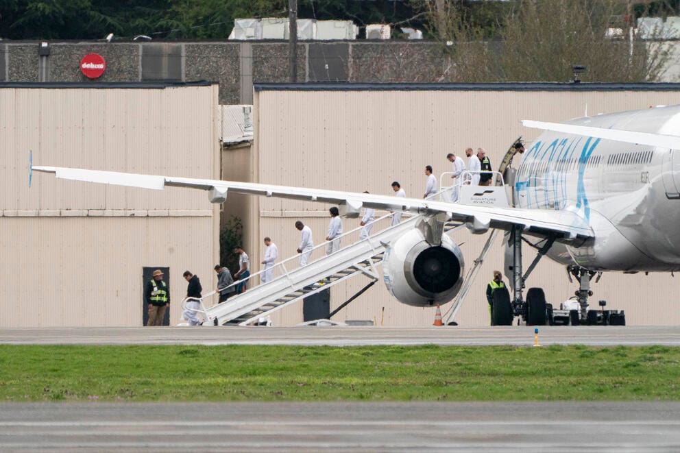 Detainees in shackles disembark from a plane