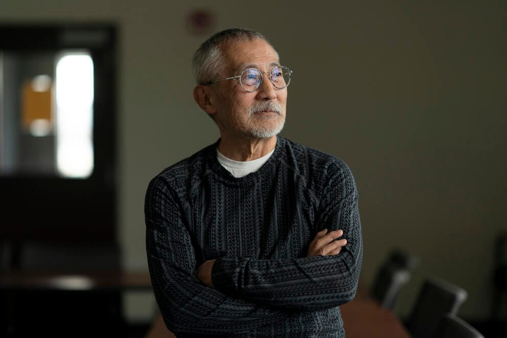 A man looks out to the window inside King County International Airport in Seattle. He's wearing wire glasses, and a gray sweater.