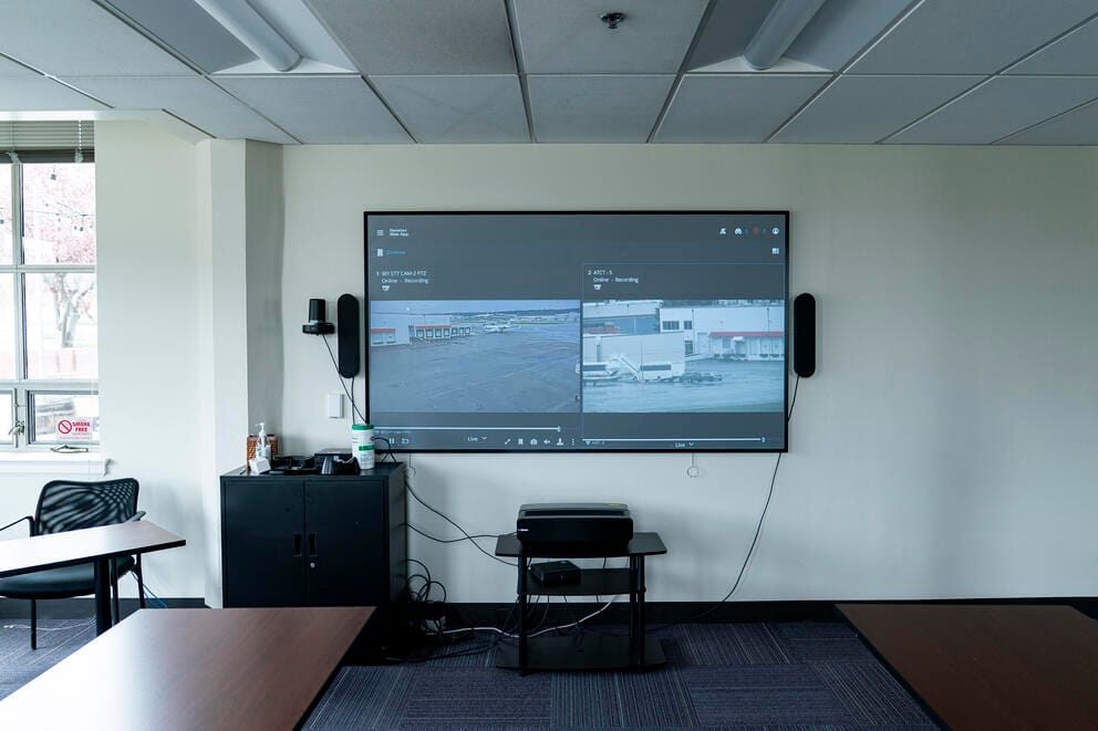 A monitor on a wall shows camera views of the plane loading area